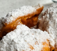Fresh beignets come out of the fryer, topped with powdered sugar
